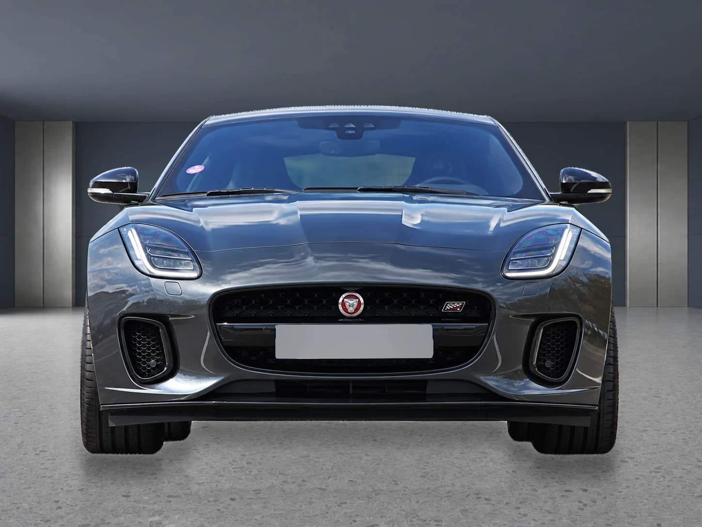 Prepared front view of the gray Jaguar F-Type in a neutral showroom with its license plate masked