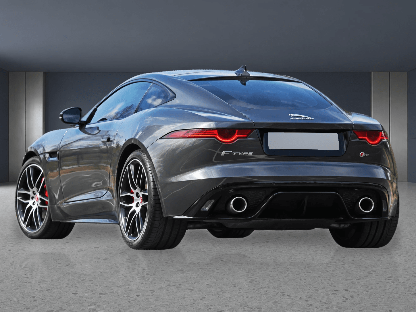 Prepared gray Jaguar F-Type in a neutral showroom from the rear three-quarter with its plate masked