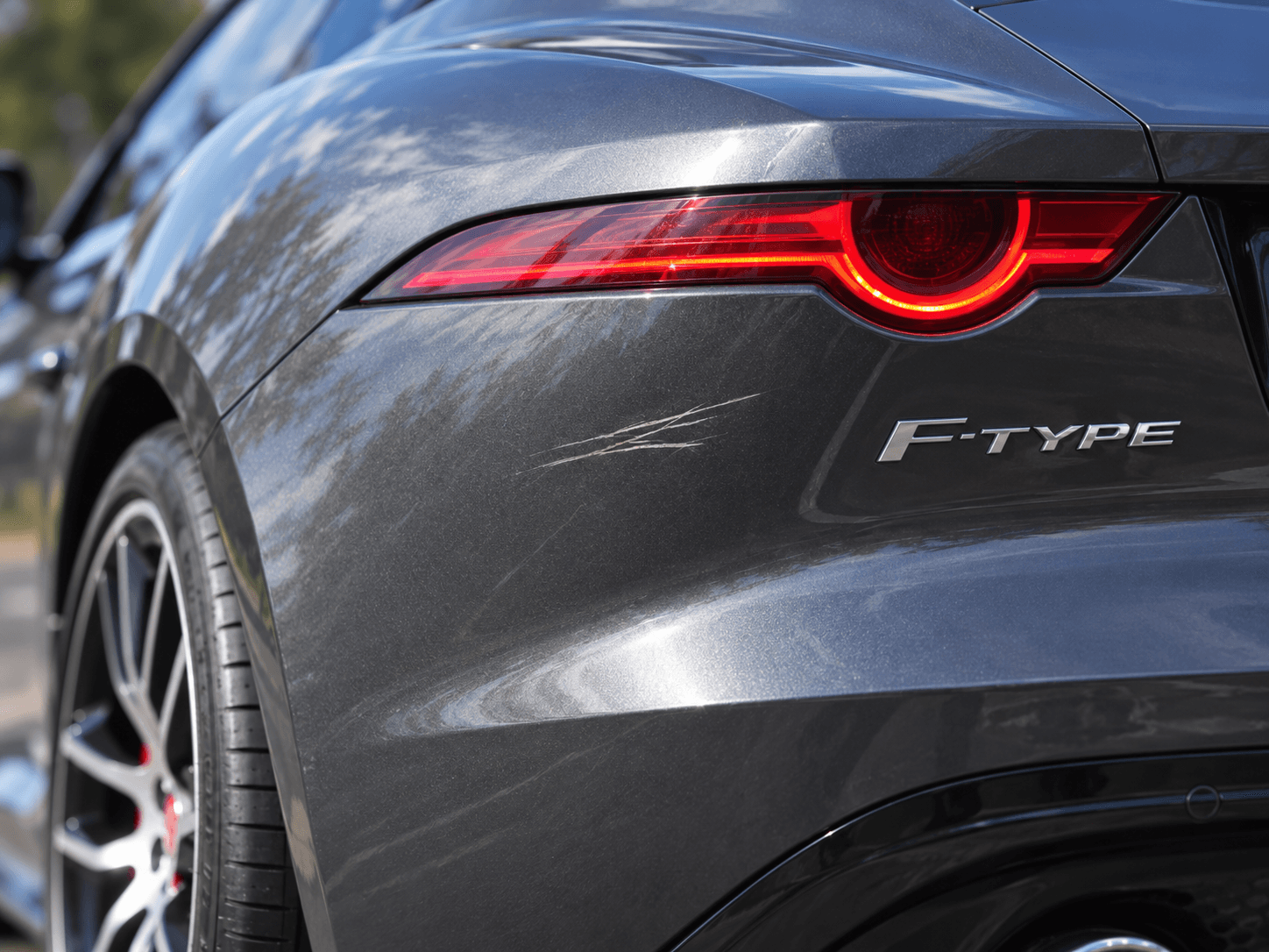 Close-up of scratches below the left rear light of a gray Jaguar F-Type